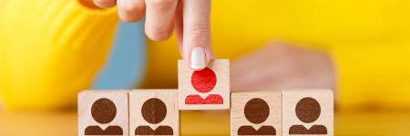 person picking a block with a red silhouette of a person out of a lineup of 4 blocks with black sihouette people