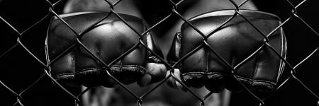 black and white photo of a man's hands with boxing gloves standing behind a fence