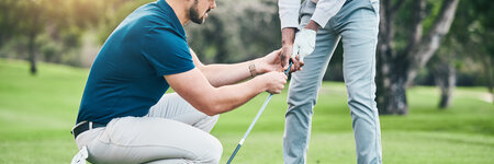 male golf instructor crouched down helping someone with their form